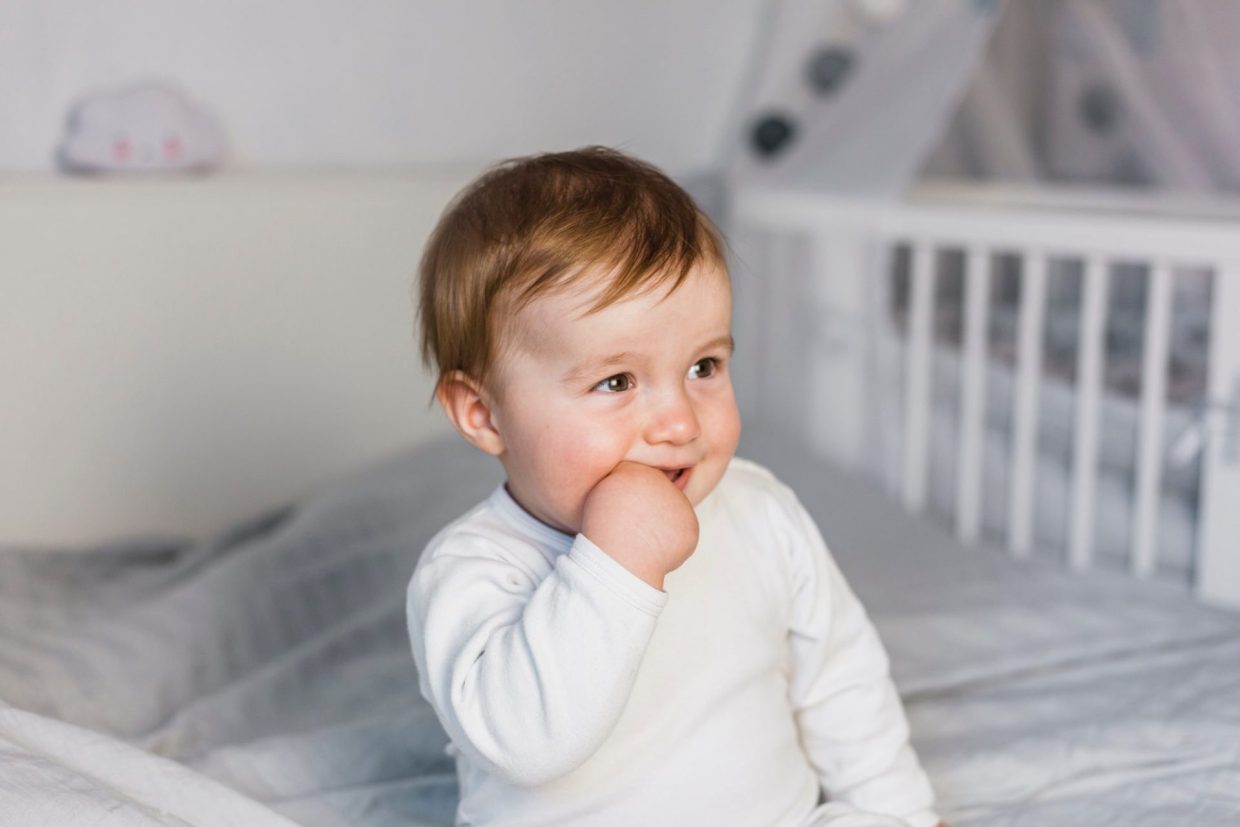 A baby with a finger in their mouth smiling